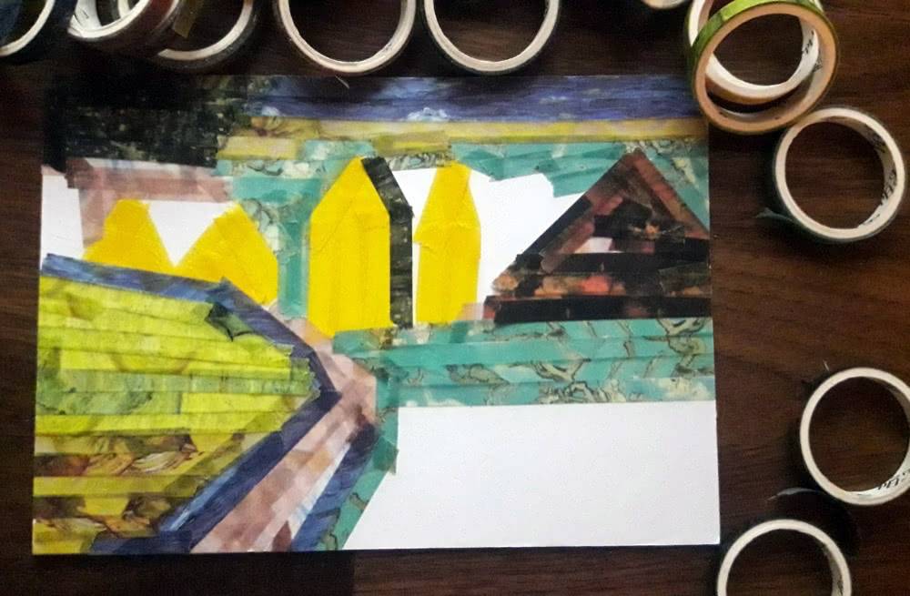 Third step of a washi tape postcard, with larger areas of sky, hills, fields and houses filled in using many torn pieces of washi tape.