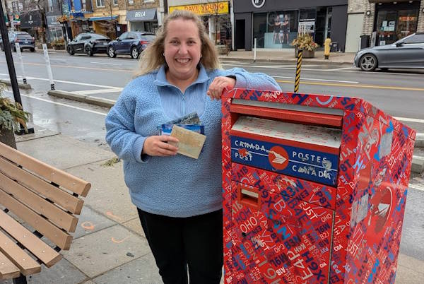 Rebecca with her local mailbox, a brightly coloured Canada Post mailbox