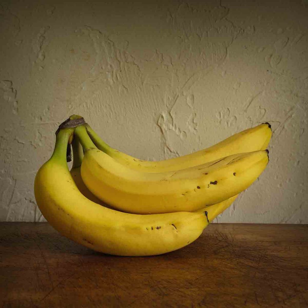 Close-up of bananas on wooden table against wall - StockFreedom