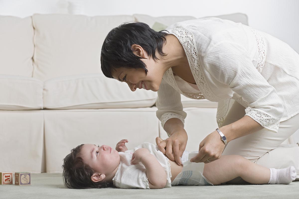 Mother changing baby's diaper on the living room floor StockFreedom
