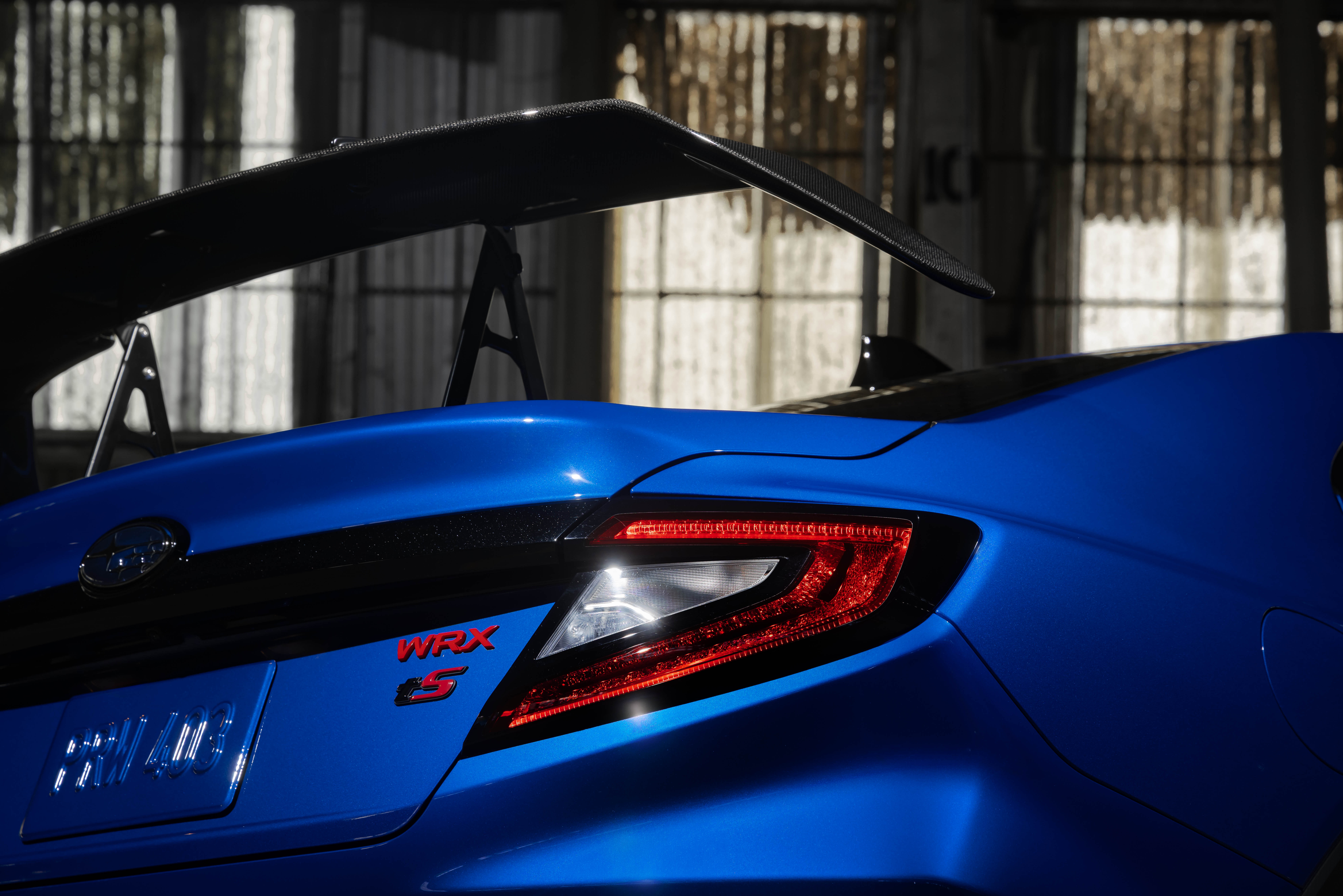 Teaser photo of the 2027 Subaru WRX tS rear quarter panel in blue, showing a large pedestal-mounted rear wing above the trunk lid