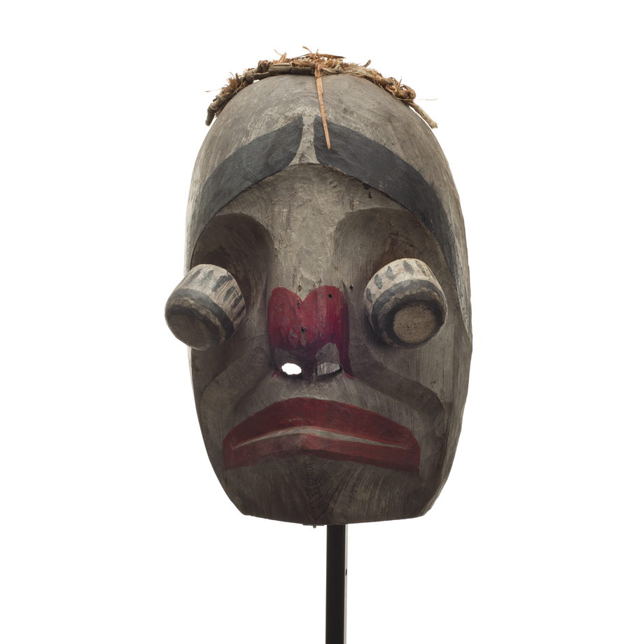 Un masque d'imitateur Atłakima, visage blanc, yeux globuleux articulés, lèvres et narines rouges, épais sourcils noirs, frange d'écorce de cèdre.