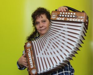 A woman faces the camera, holding up an accordion outstretched in front of her. This is Eva Ybarra.