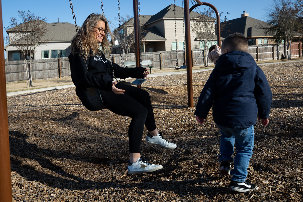 a woman sitting on a swing with her child standing in front of her