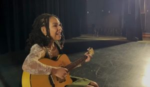 a teen girl playing a guitar onstage