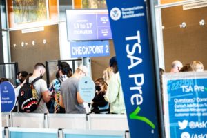 a TSA Pre banner in the foreground, with a line of people beyond