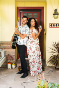 a man holds a guitar and a woman holds a microphone on a front porch