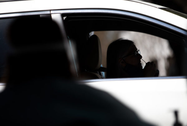 a covid tester, seen from the back, and a car at a COVID testing event.