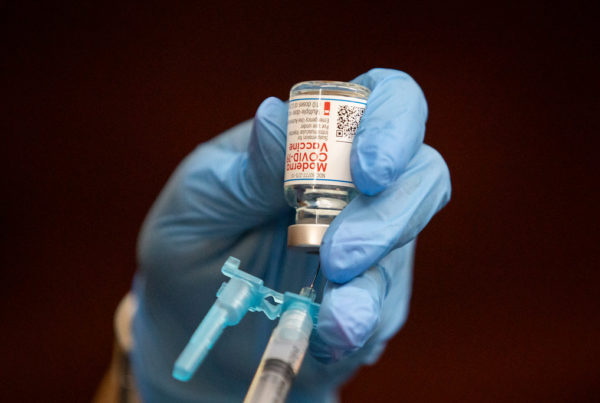 A hand holds a vaccine container that's connected to a vial.