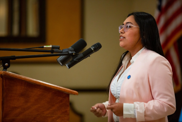 Candidate Jessica Cisneros stands at a podium, speaking into a microphone