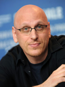 a close-up photo of Oren Moverman. He looks at the camera. He is wearing a black shirt and glasses.