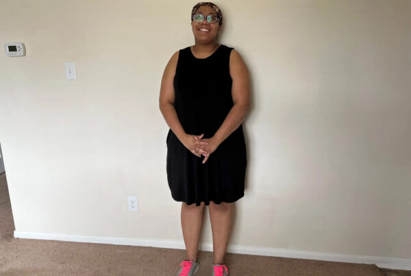 A woman stands facing the camera and smiling in front of a blank wall. This is Manda Rogers.