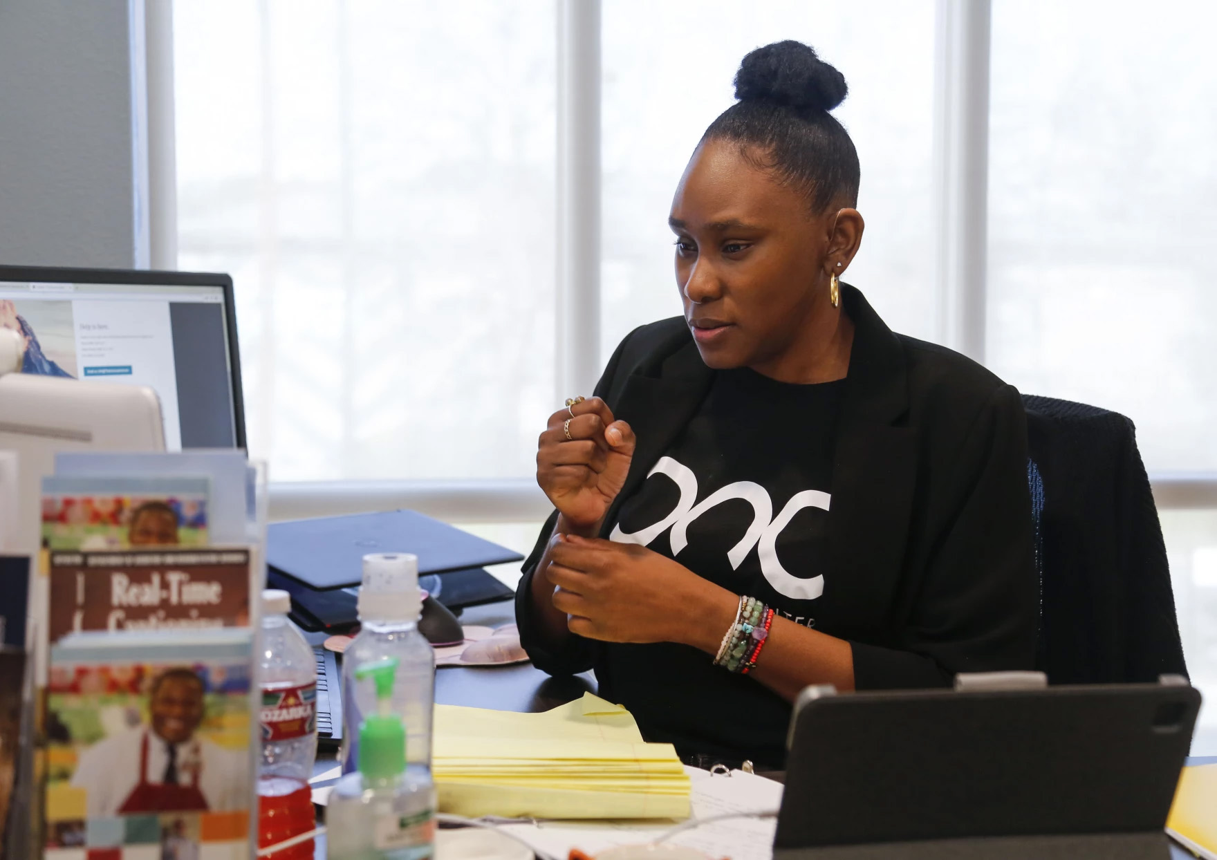 A woman is sitting at her desk, gesturing in sign language at the monitor in front of her. This is Bianca Walker, a deaf and hard of hearing specialist at the Deaf Action Center.
