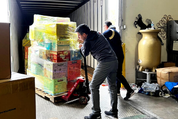 A man pushed a pallet of boxes several feet high and wrapped in plastic shrink rap into a truck.