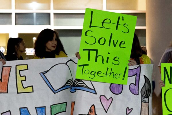 A poster that says "let's solve this together!" is held up at a rally against potential school closures