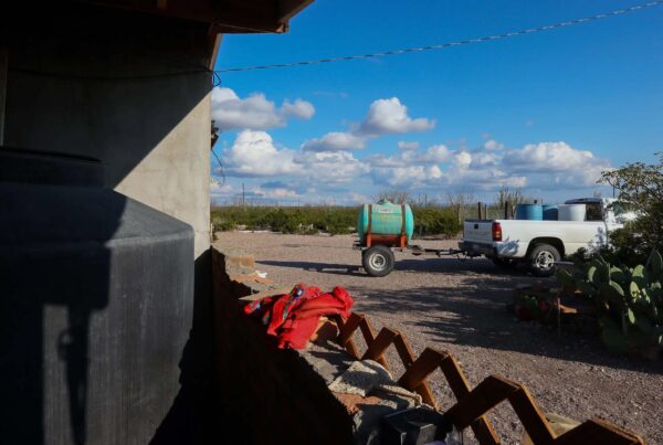 A portable water tank is hitched to a white pickup truck that has large plastic barrels in its bed