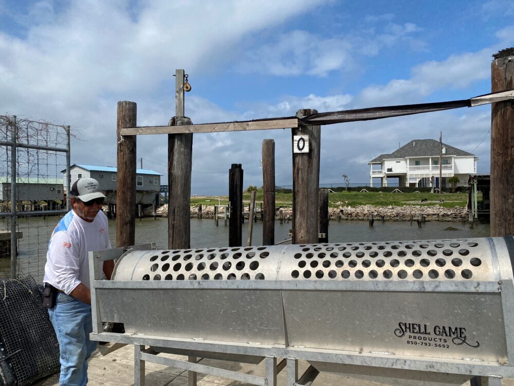 A large, metal machine with several holes on top is seen. A man to the left works the machine.