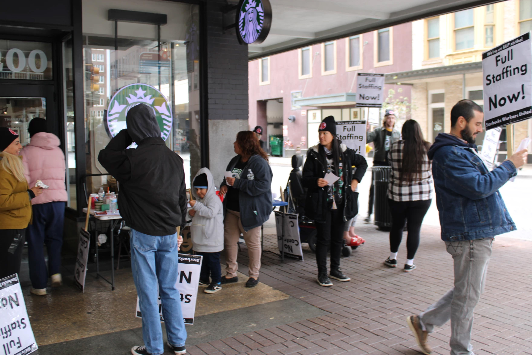A group of workers are seen picketing outside a Starbucks location. The most prominent signs seen read 