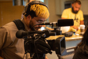 a young man wears headphones and looks through a video camera