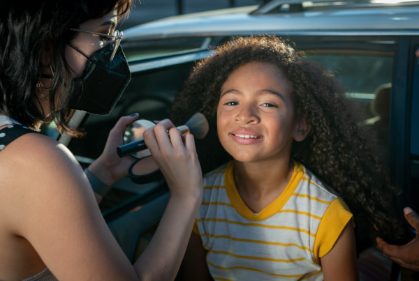 A makeup artist wearing a face mask touches up the makeup on a child actor in the film "I'll Be There."