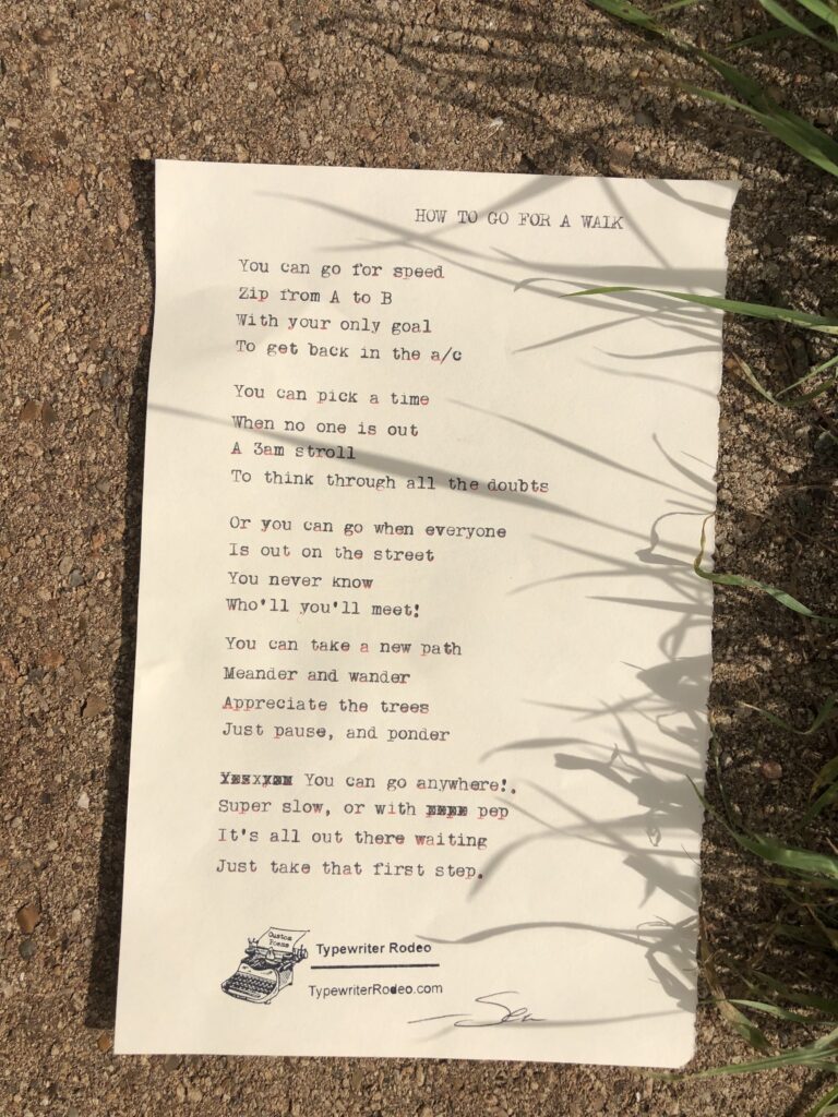 A photo of the typewritten poem on a torn half-sheet of light yellow paper. The paper is on a sunny piece of sidewalk with the shadows of blades of grass on it.