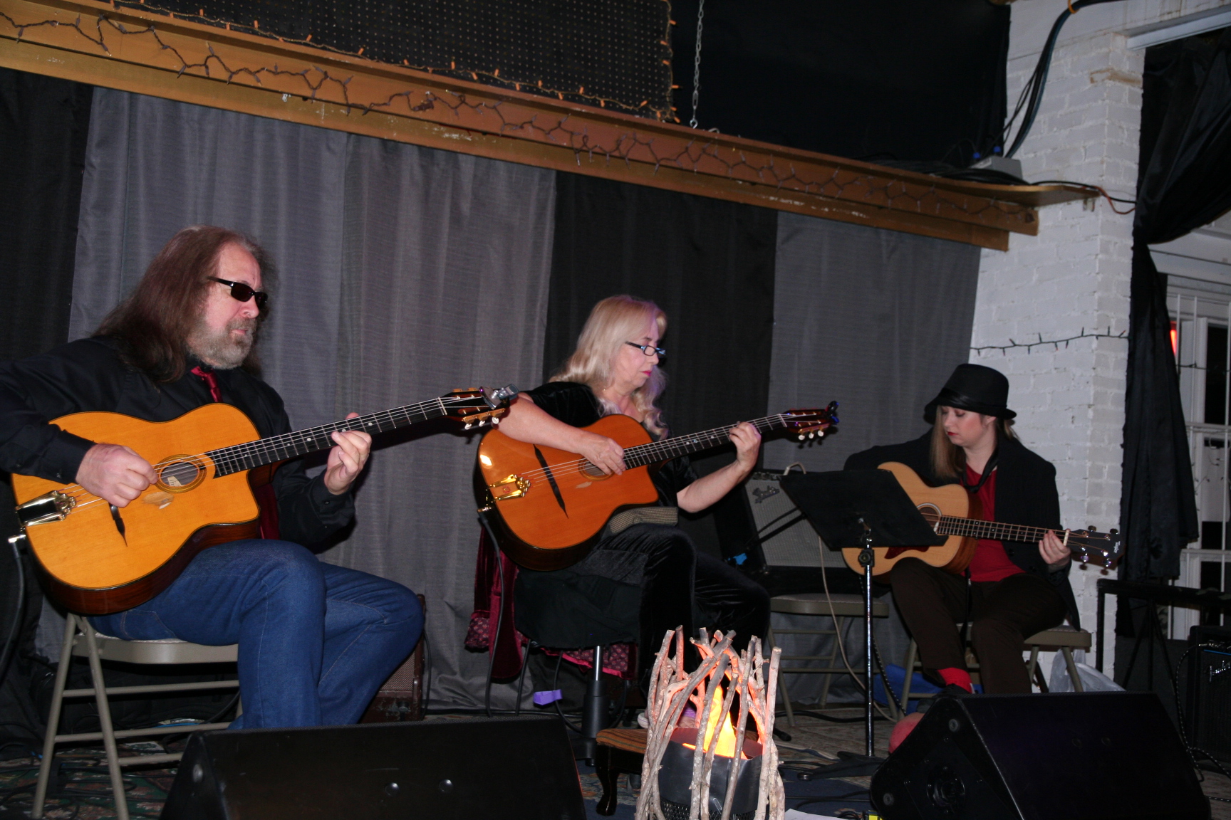 Three seated musicians play on acoustic guitars.