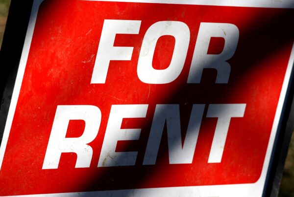 A red sign with white letters reading "For Rent." There is a shadow across the sign.