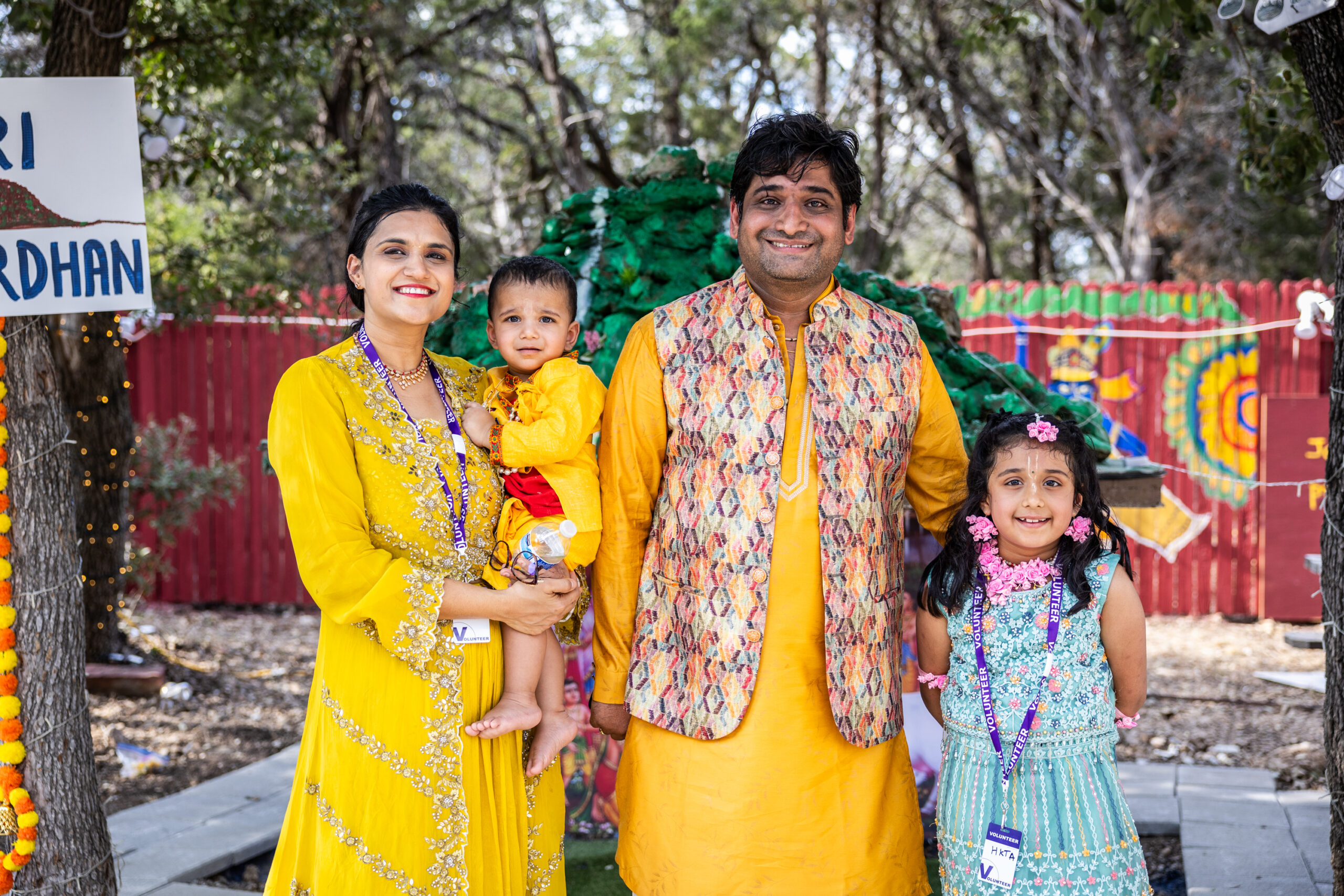 A family of four dressed in traditional garb for the Krishna Janmashtami festival pose for a photo. The wife holds a young child while a young girl stands next to the father. They are Neha and Umesh Tiwari and their children.
