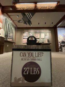 A photo of a Mexican cannon ball with a sign saying "can you lift?" It weighs 27 pounds.