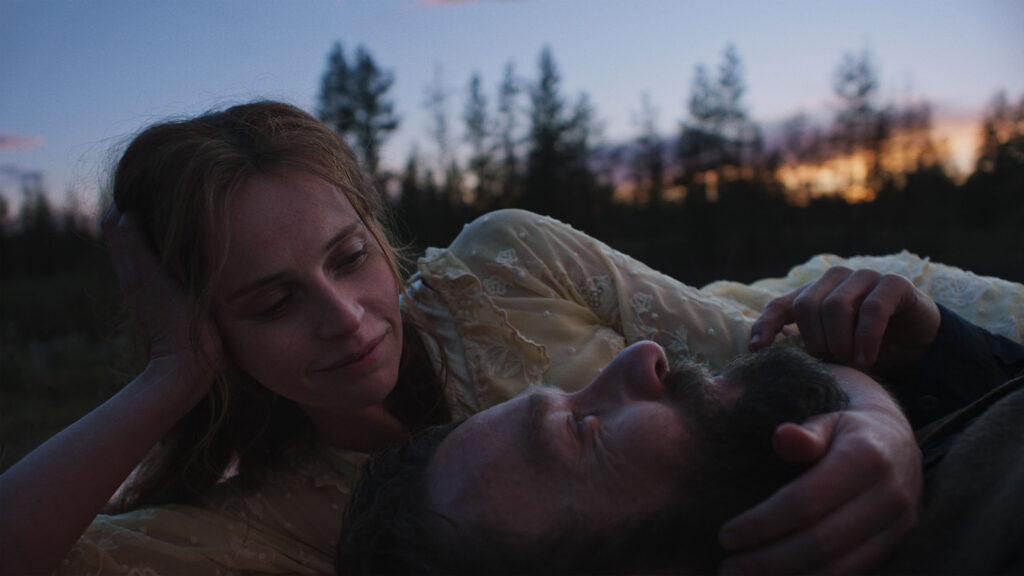A film still shows the close-up image of two actors lying on the ground outside.