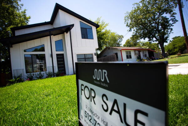 A residential "for sale" sign is seen in the yard outside a white house