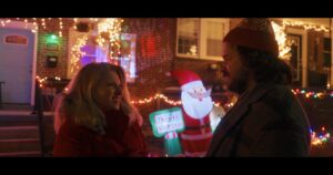 Two people have a conversation with Christmas decorations behind them.