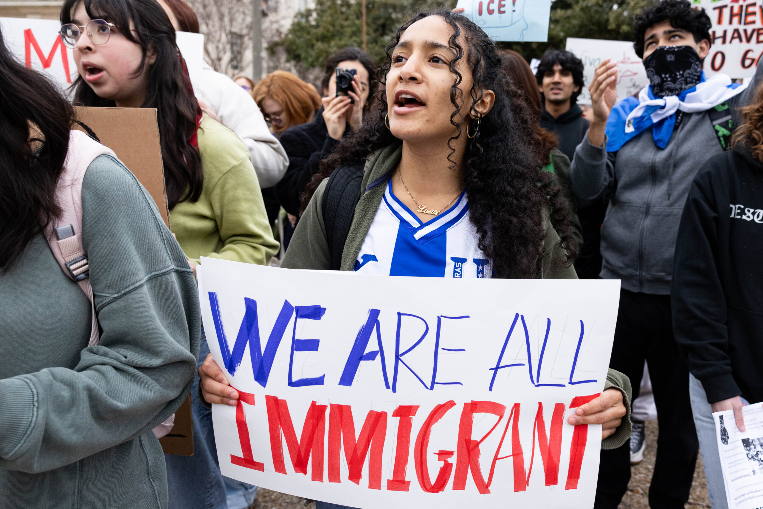 A young woman chants at a protest holding up a sign reading 