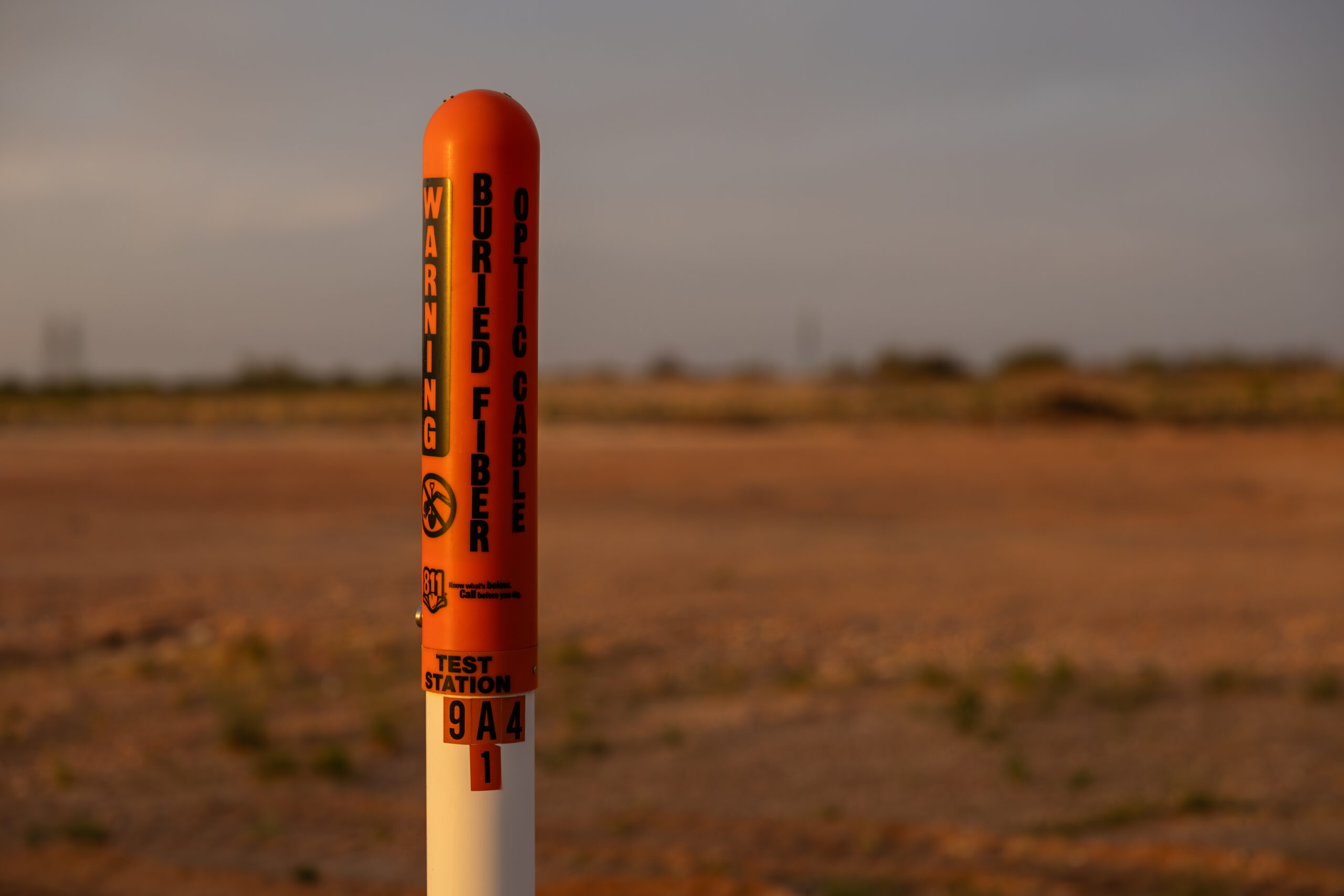 A white and orange pole is seen in the foreground outdoors during sunset. Words written on black on the pole read 
