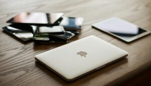A closed Apple laptop is seen on a table next to a pile of phones and tablets