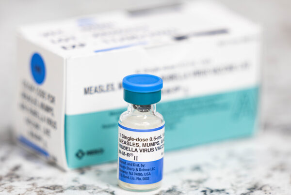 A closeup of a medical vial with a label that reads "Measles, Mumps, and Rubella virus vaccine"