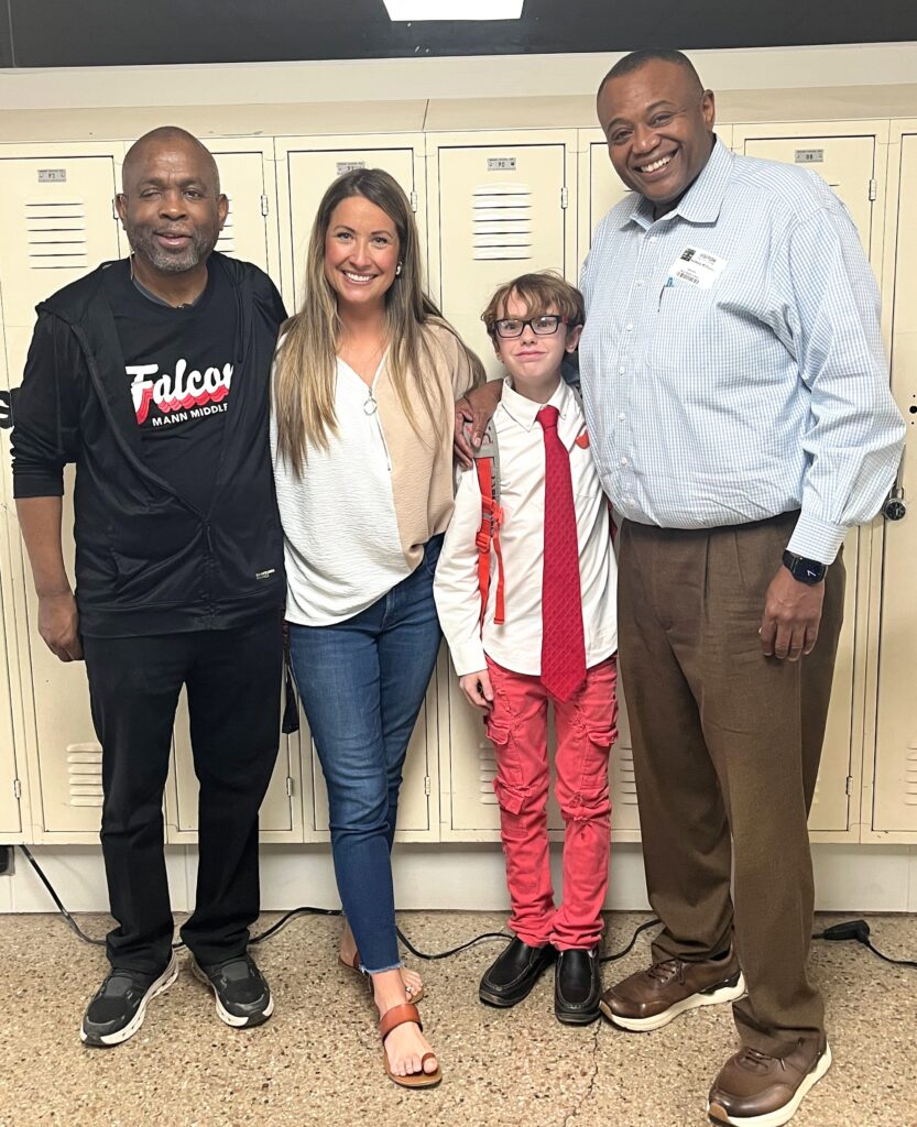 Three adults and a child pose for a photo in front of tan lockers.