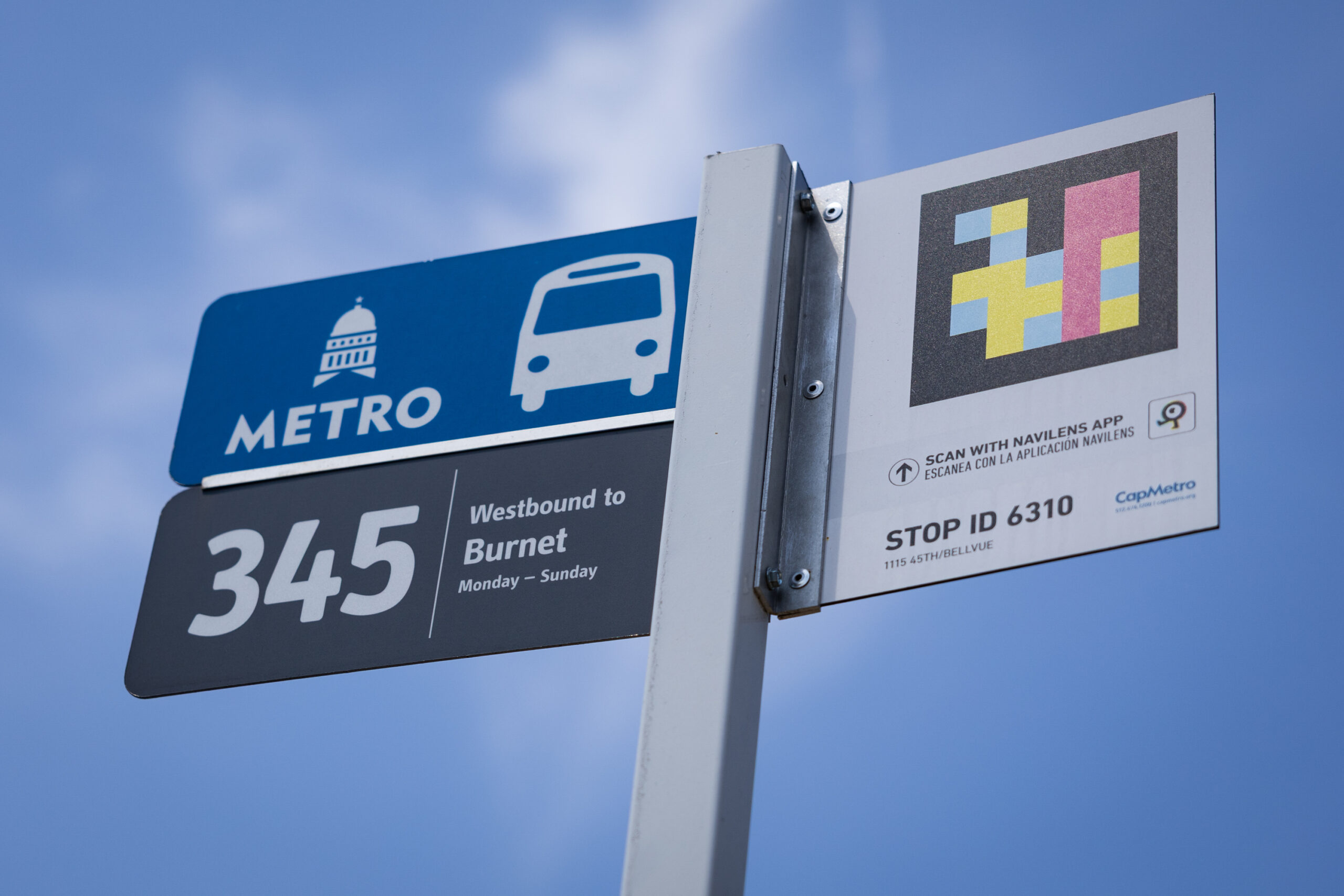 A bust stop sign is seen, with one part of the sign advertising the Navilens App.