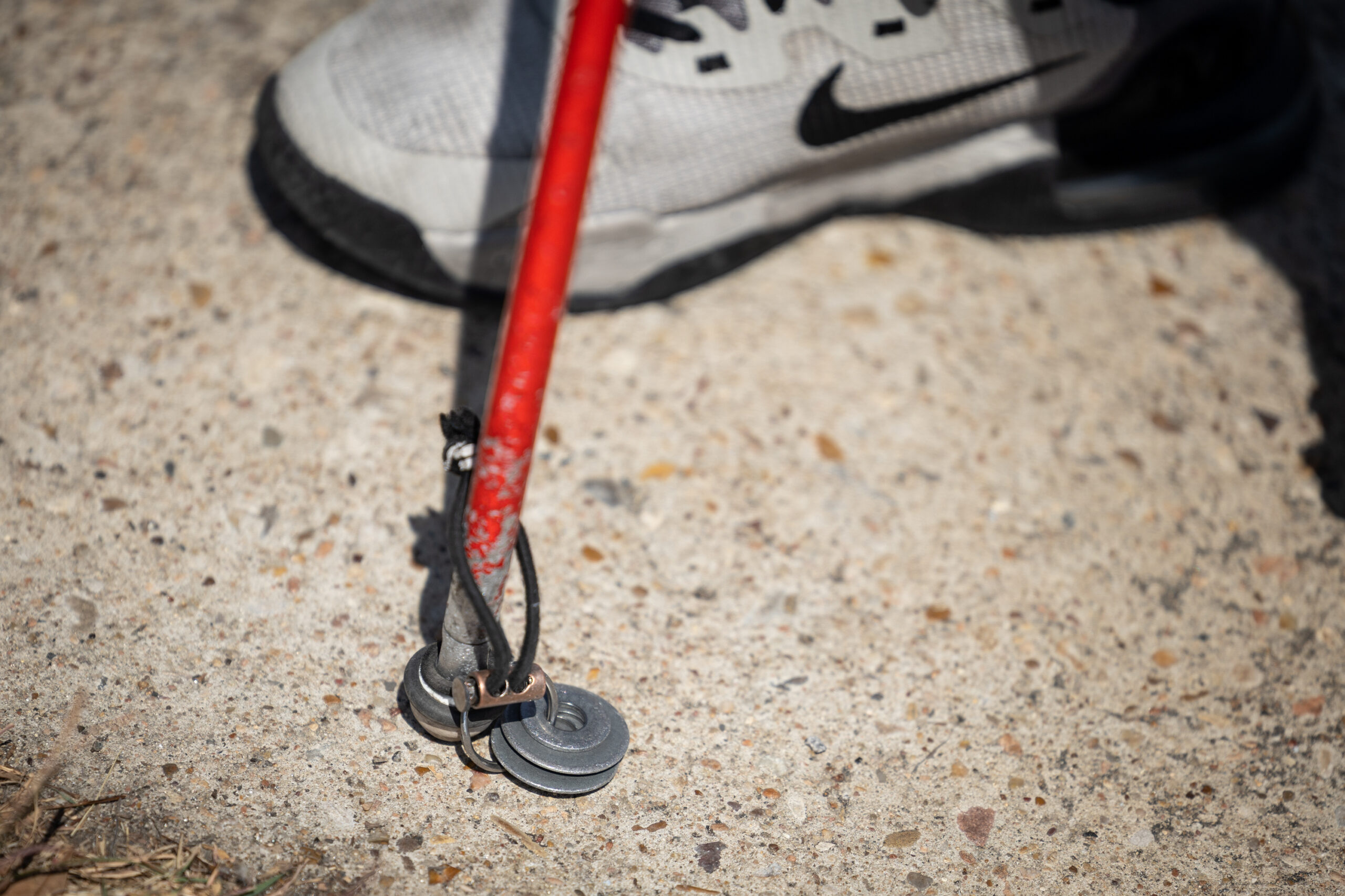 A close up of a cane tip on pavement, showing three metal washers attached to the bottom with a cord.