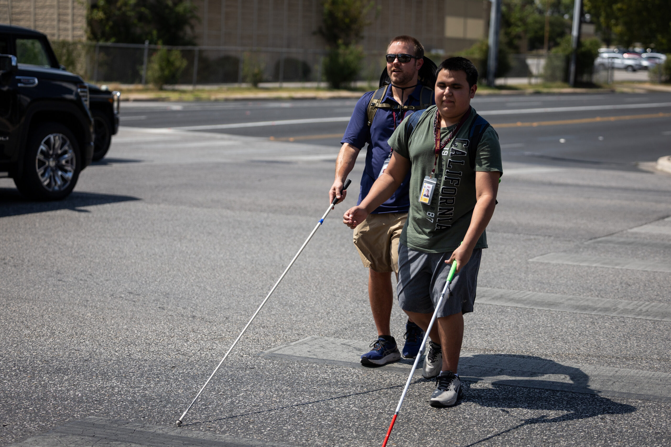 Two men walk across a crosswalk using their white canes. This is Drew Bernet and Oscar Garcia.