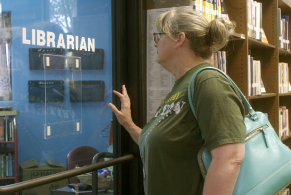 A photo of Baker looking through an internal window into an office. The word "librarian" is printed in white on the window.
