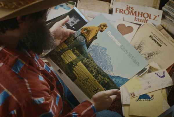 A still image from the film "The Man with the Big Hat" shows a person looking at the obscure debut album of Steven Fromholz.