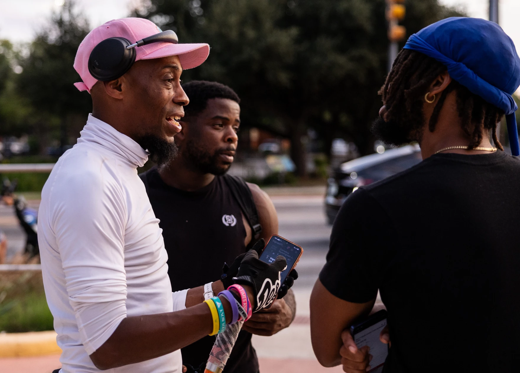 A man wearing headphones stops to talk with other people who have come by his street corner.