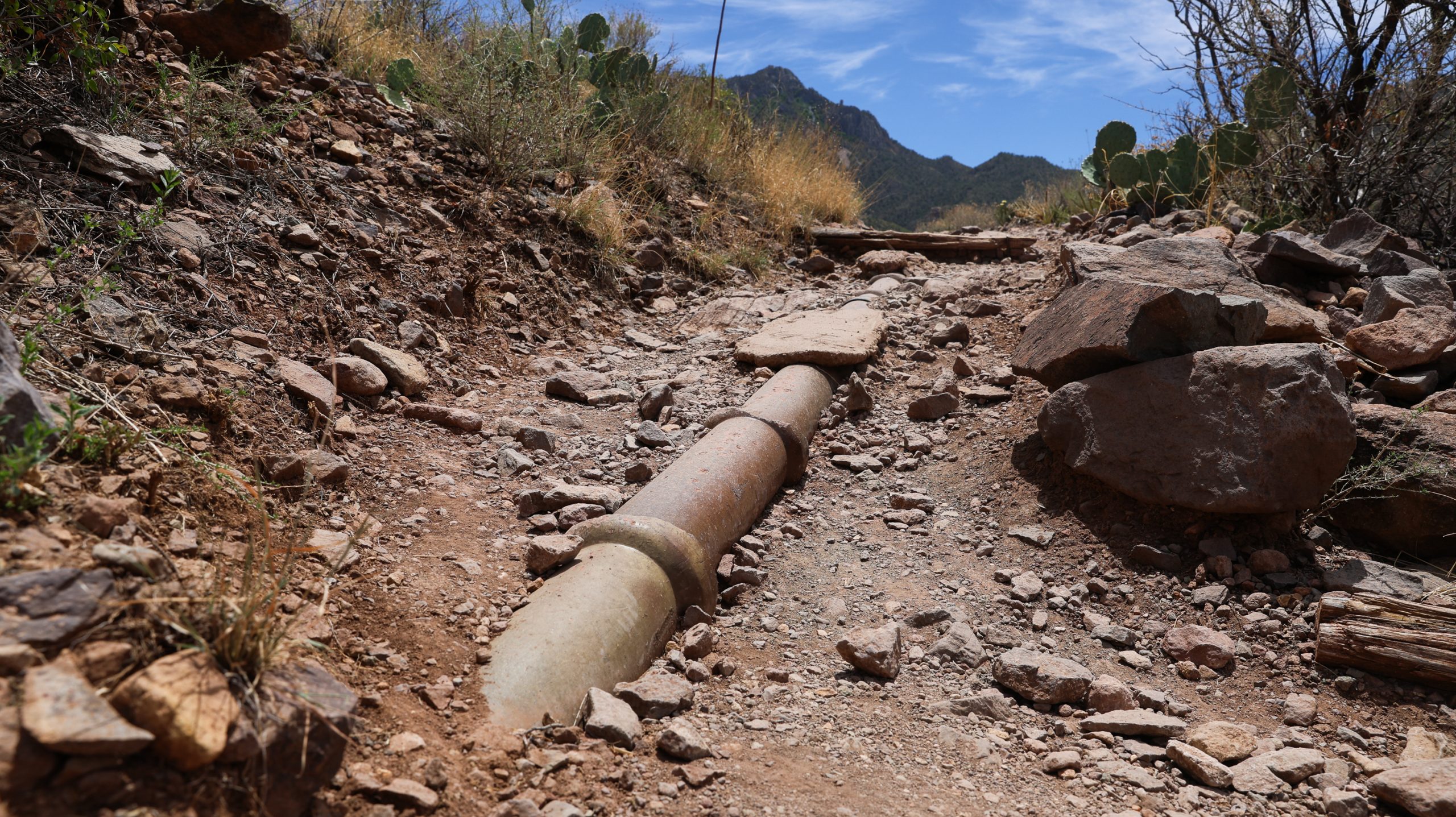 A section of exposed pipe is seen partly buried in rocky ground.