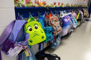 A row of childrens' backpacks hanging on wall hooks