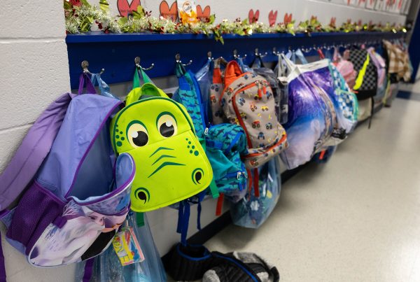 A row of childrens' backpacks hanging on wall hooks