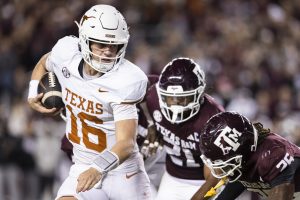 A Texas quarterback in a white uniform with a burnt orange 16 on it tries to avoid being tackled by two Texas A&M players in maroon.