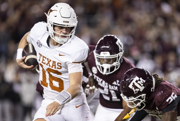 A Texas quarterback in a white uniform with a burnt orange 16 on it tries to avoid being tackled by two Texas A&M players in maroon.