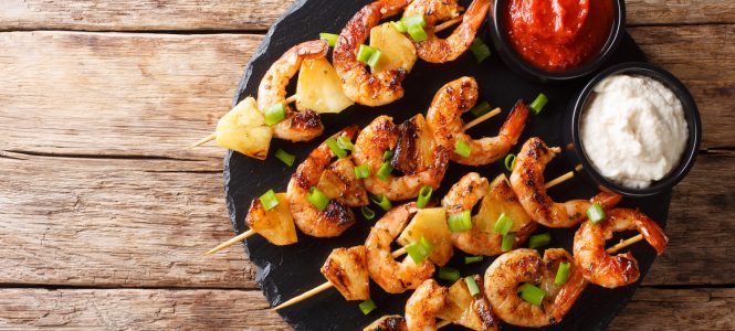 Shrimp Kabobs with Pineapple – Grillin’ on the Fourth of July Fresh kebabs made from shrimps and pineapple slices decorated with green onions served with sauces close-up on a slate plate. Horizontal top view