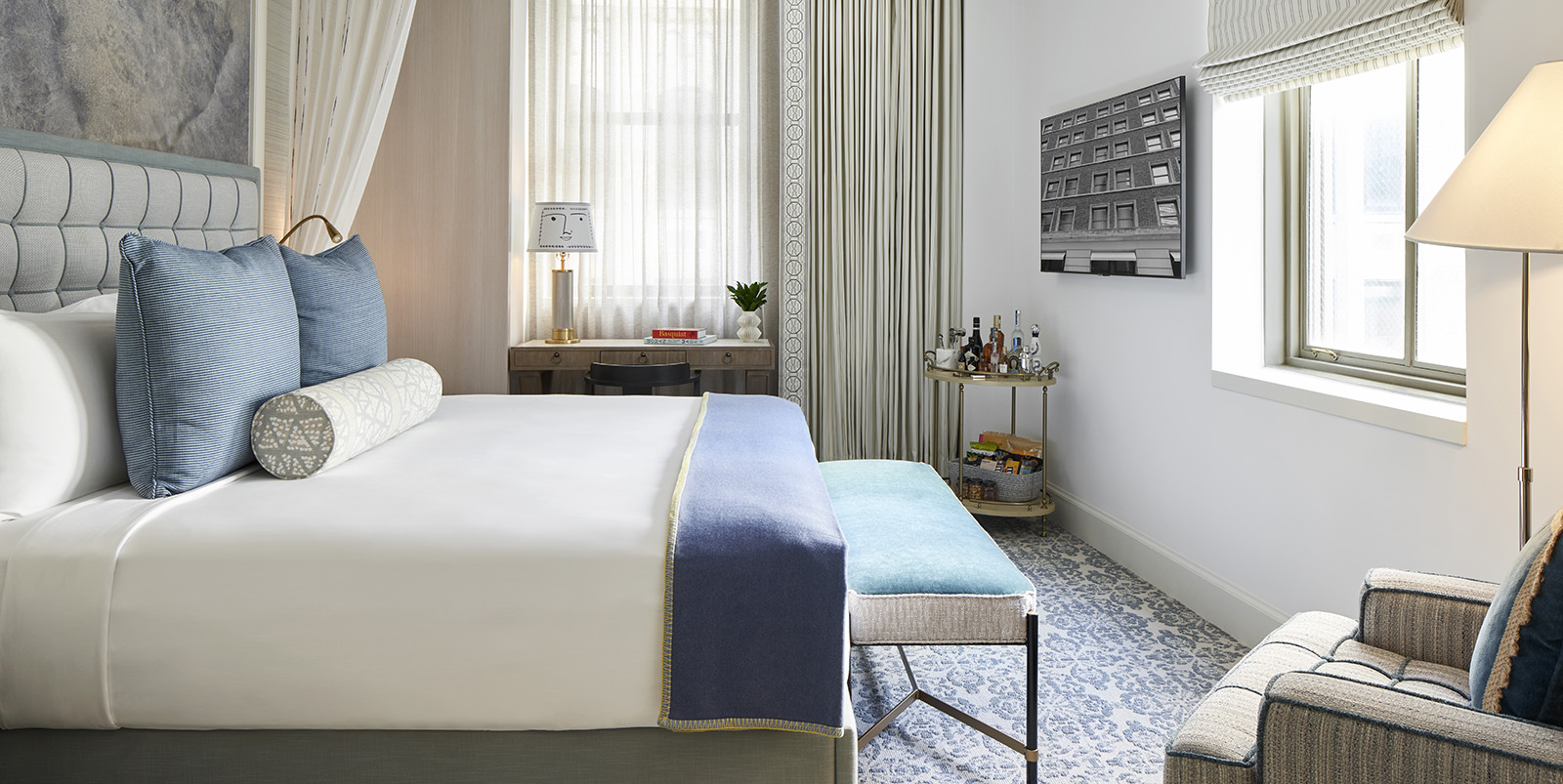 A luxurious hotel room with a king-sized bed, comfortable seating area, and large windows.